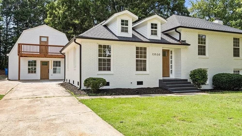Front elevation of a white painted brick split-level in Matthews, with charcoal architectural shingles running across the main hip roof, the two front dormers, and the covered entry.