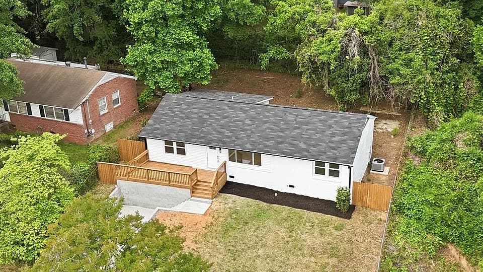 Overhead view of the finished roof, charcoal architectural shingles covering the full main plane and the lower rear section, with the neighboring home's older brown roof alongside for comparison.