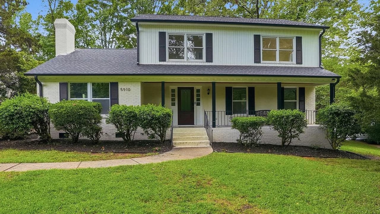 Front elevation of a painted-brick two-story on Grosner Place, weathered-grey architectural shingles running across the upper gable roof and the wide low-slope plane that covers the full-width front porch.