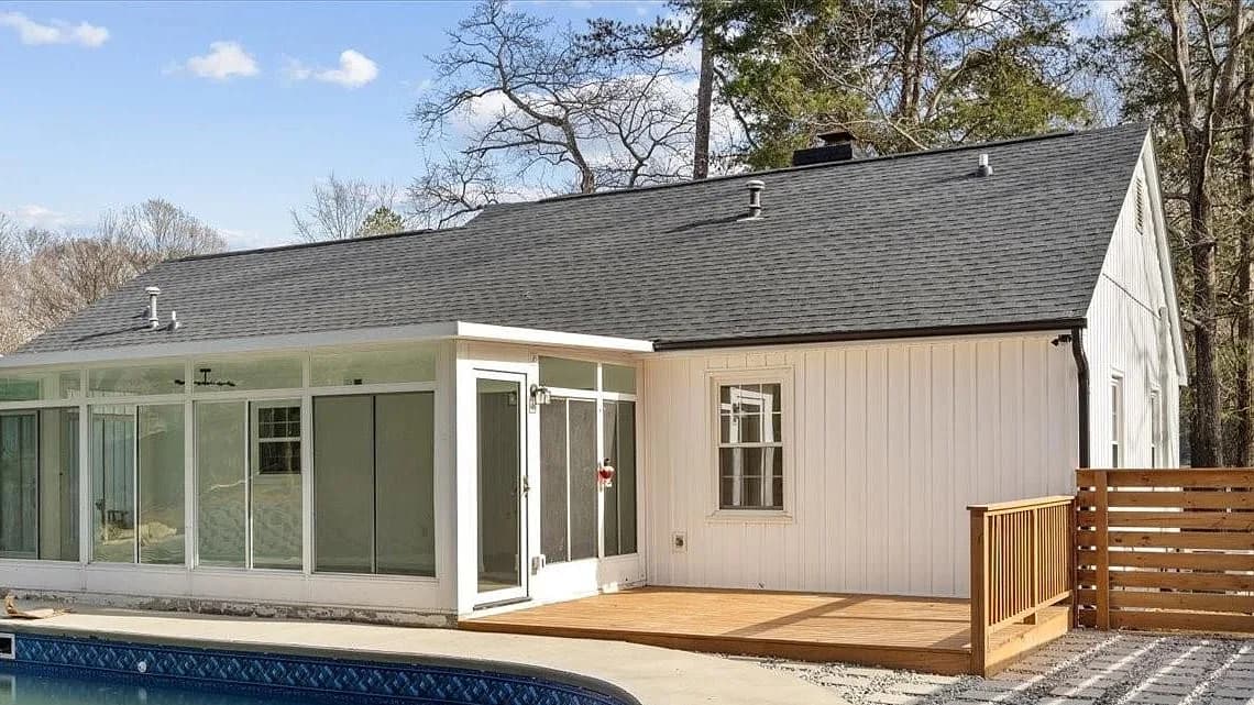 Rear elevation after the reroof, with charcoal architectural shingles running the full length of the main slope past three plumbing vent boots and the chimney chase, down to a black drip edge above the sunroom.