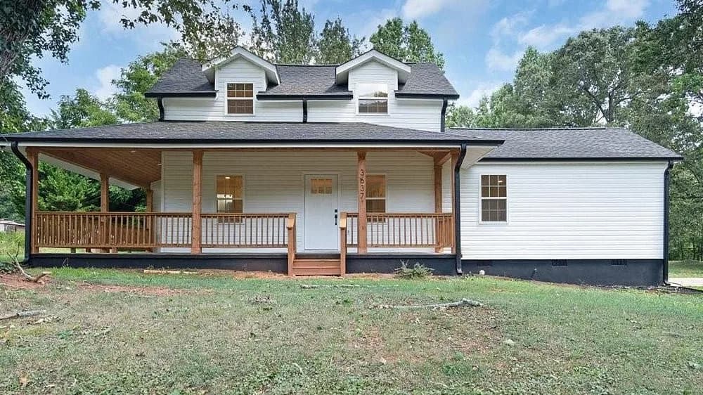 Front elevation of a white 1940 farmhouse near Lincolnton, with charcoal architectural shingles carried across the main gable, both dormers, the wraparound porch, and the side wing.