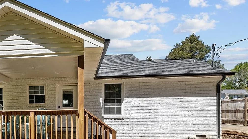 Close view of a completed Rixa roof in Charlotte where a rear covered porch meets the main roof, with the staggered laminated shingle courses, the ridge line, and the black drip edge all visible.
