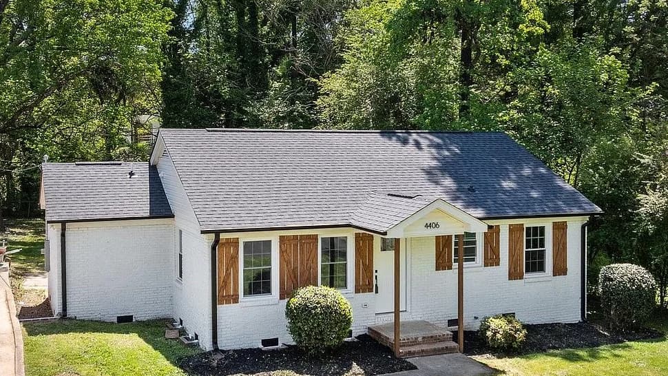 Elevated view of the finished roof with the whole charcoal shingle field visible at once, running from the hipped ridge down over the entry gable and across to the lower side wing.