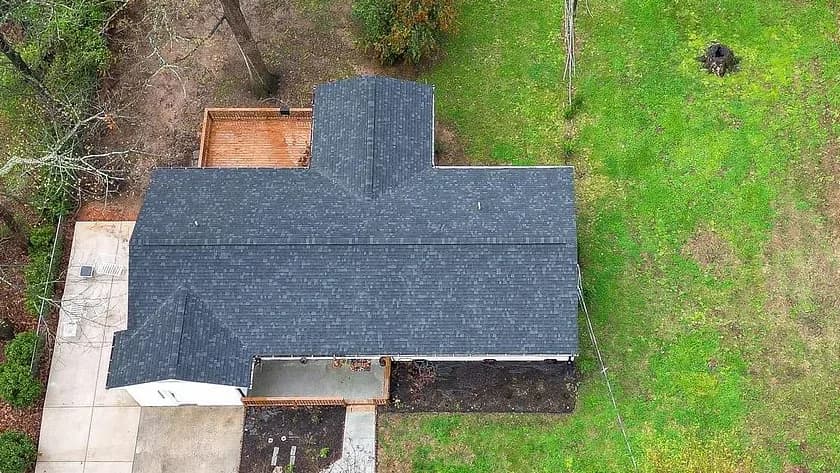 Overhead view of a finished Rixa roof in Kings Mountain: one continuous field of charcoal architectural shingles across the main gable, the rear projection and the side wing, with the ridge and the valleys cleanly cut in.